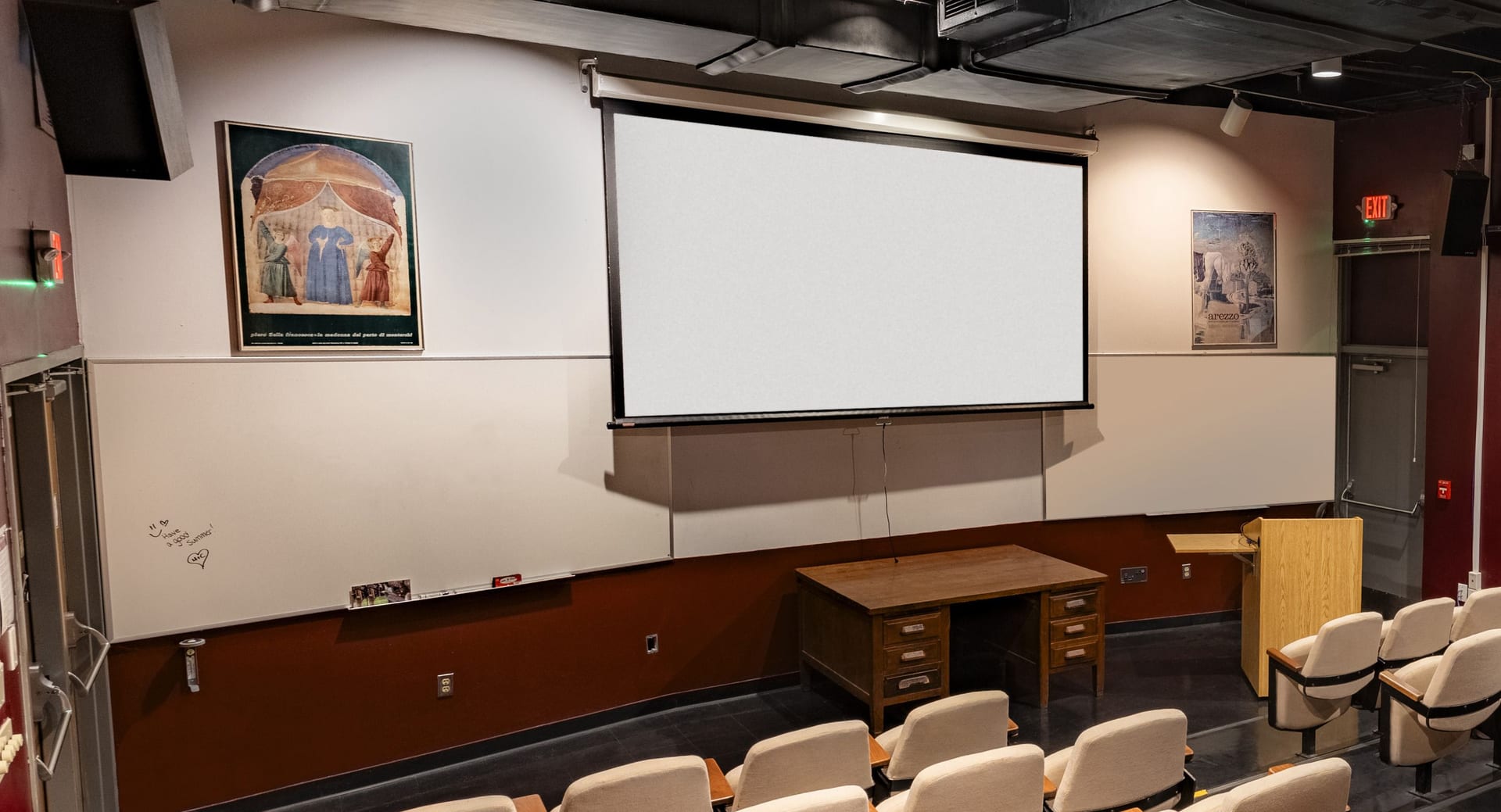 Projection screen above whiteboards, with a wooden desk and a lectern at the front of Jones 125