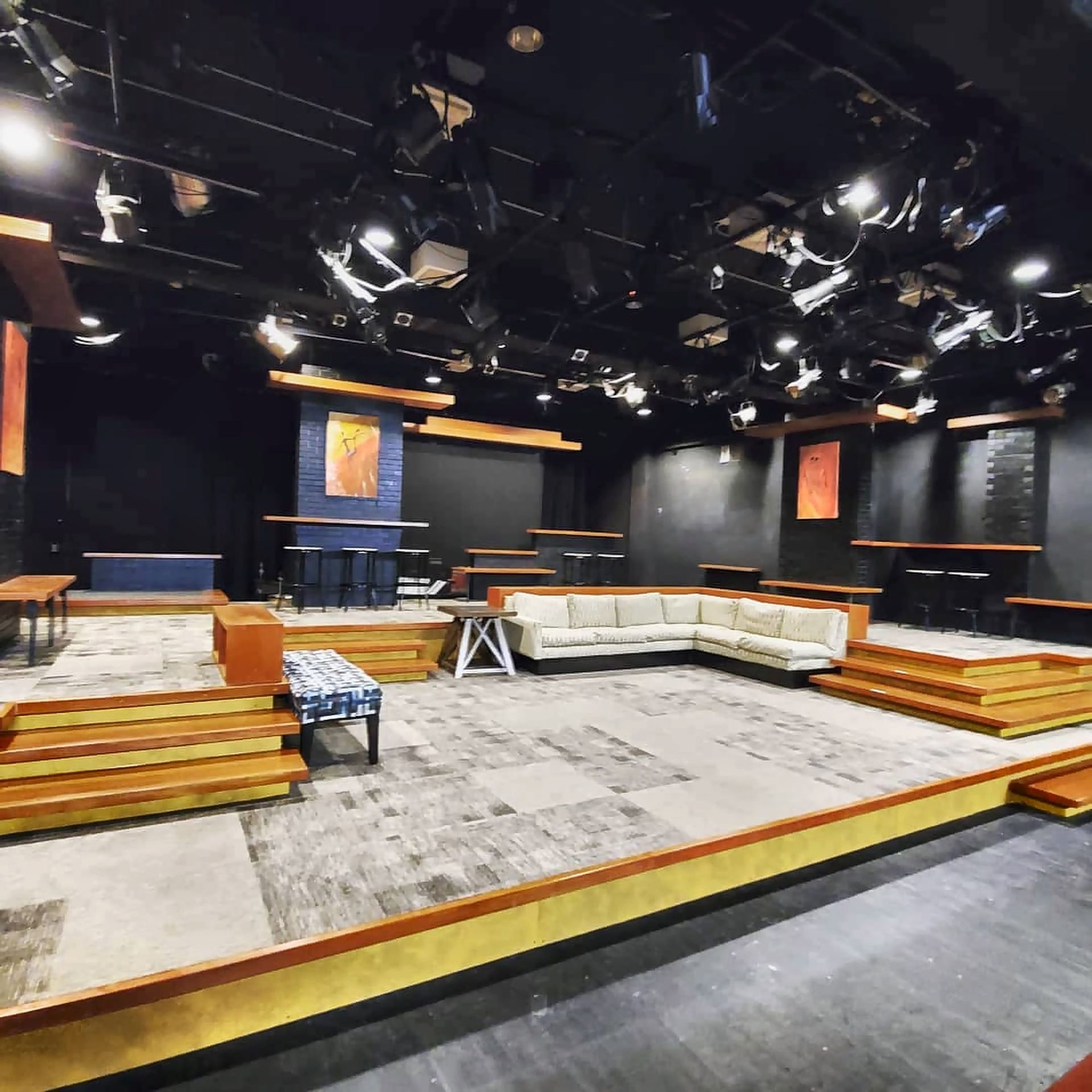 Jones 125 with a production set: carpeted platforms, wooden steps, a sectional sofa and bar stools under a grid of stage lights